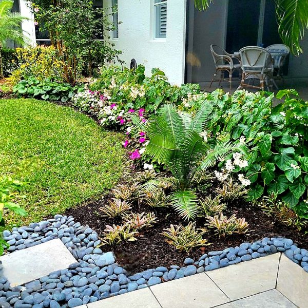 Backyard by Metis Design Love's Install porcelain pavers with beach pebble border and colorful plants